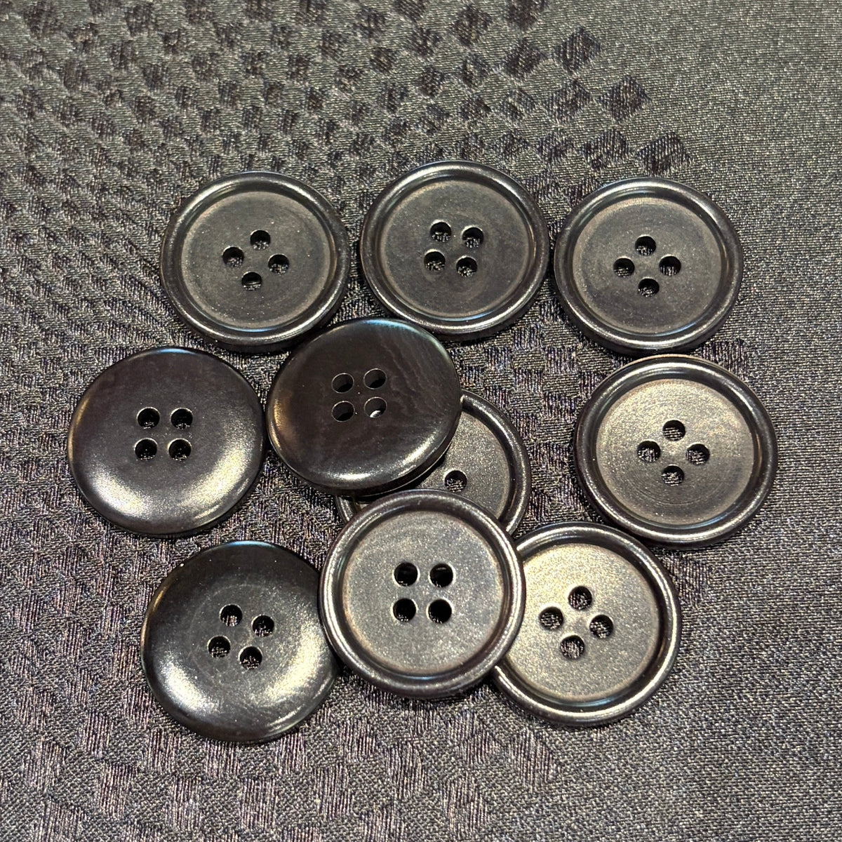 Nine black four-hole buttons arranged on a textured black fabric background.
