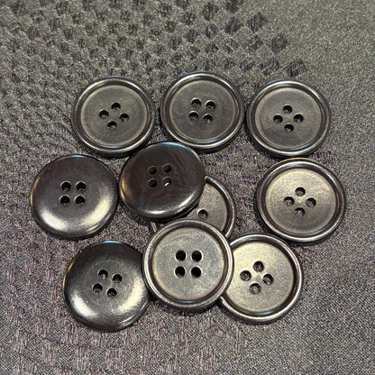 Nine black four-hole buttons arranged on a textured black fabric background.