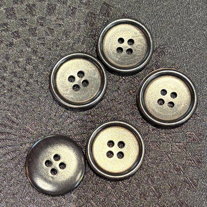 Five black buttons arranged on a textured dark gray fabric surface, photographed from above on a black background.