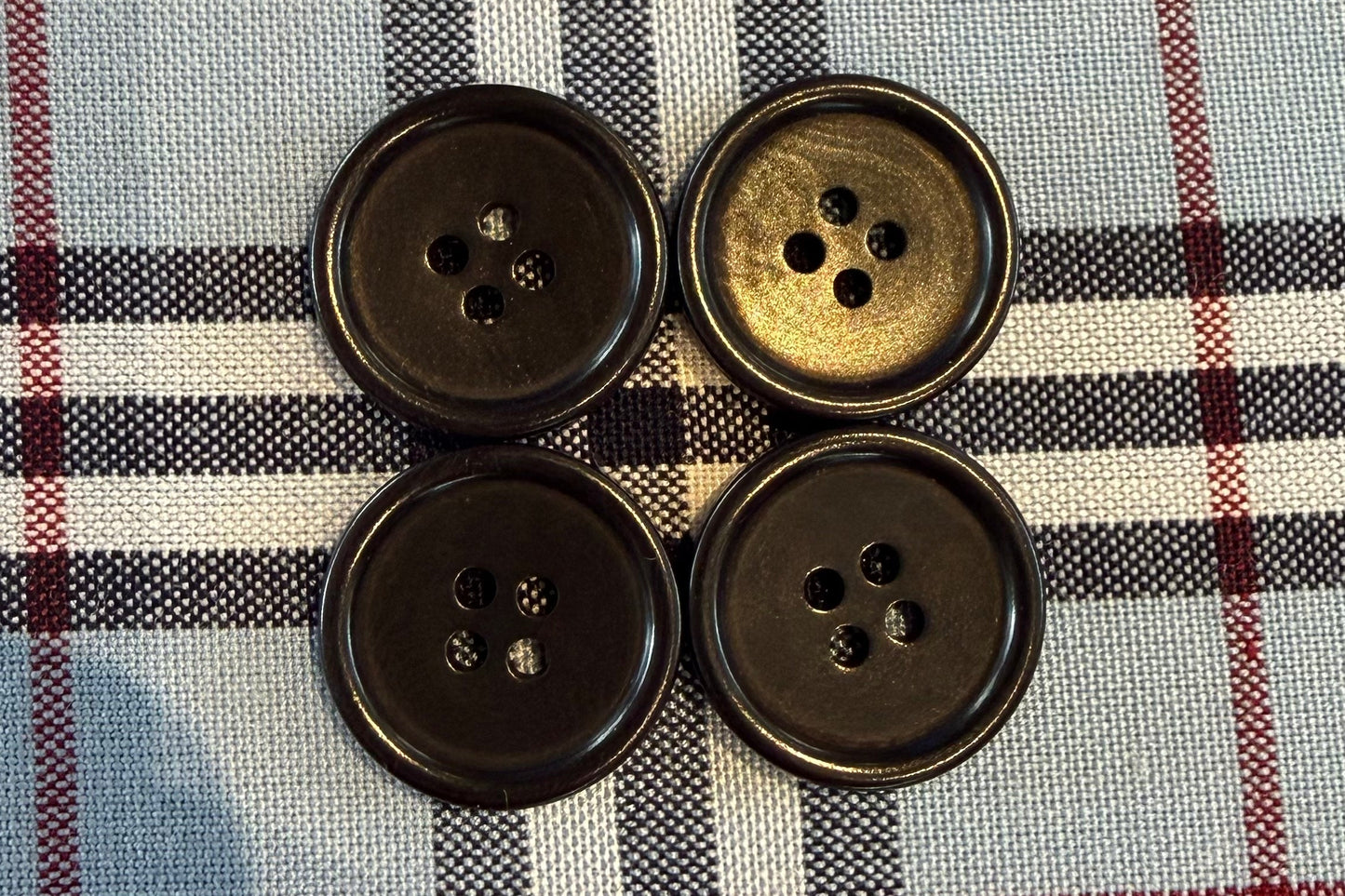 Four black buttons on plaid fabric