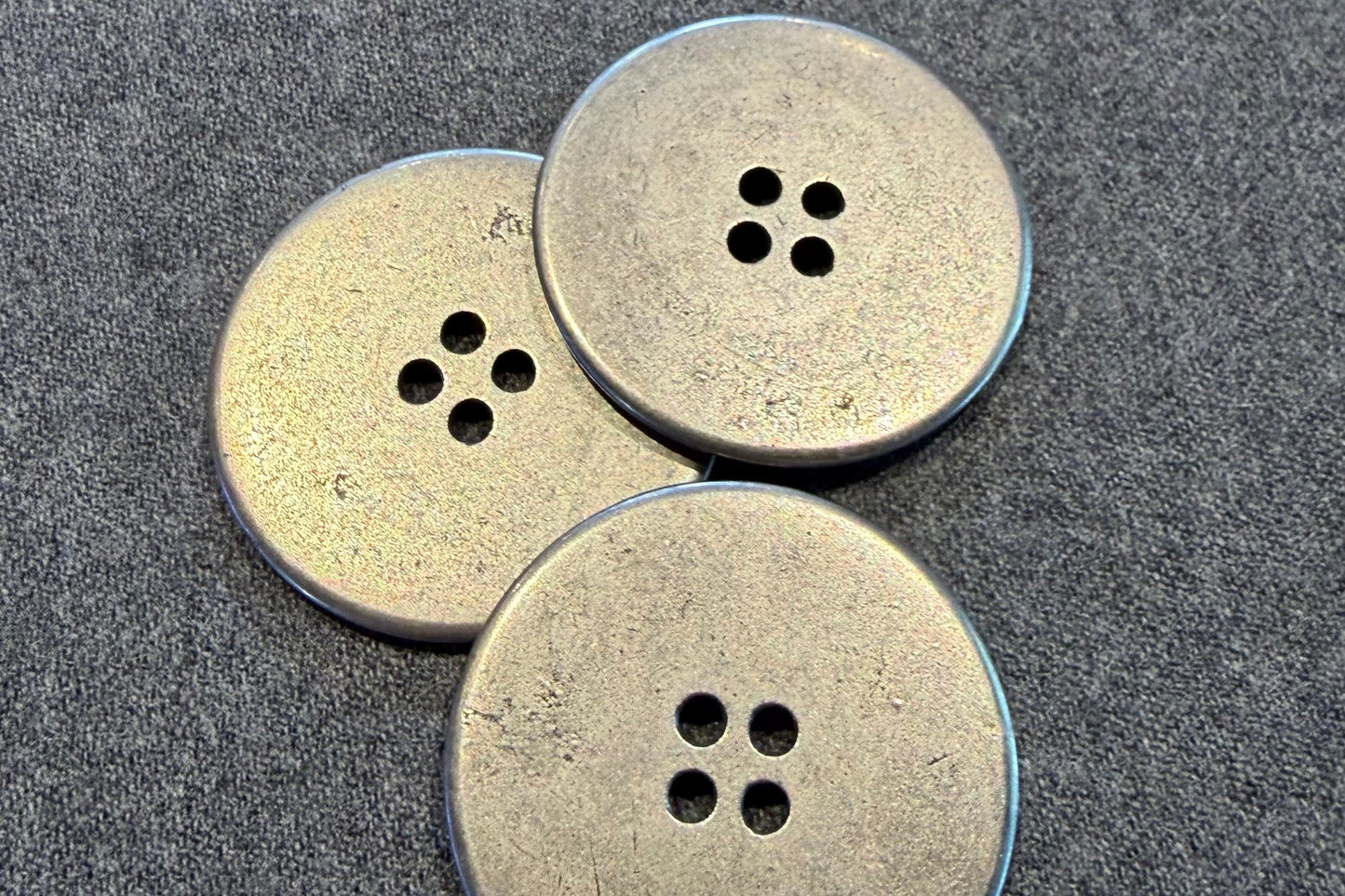 Three silver buttons with four holes on a textured surface