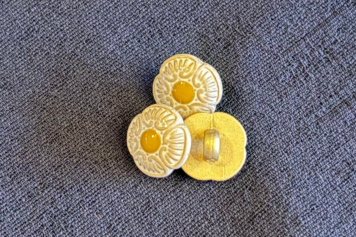 Three decorative buttons with floral patterns on a textured surface