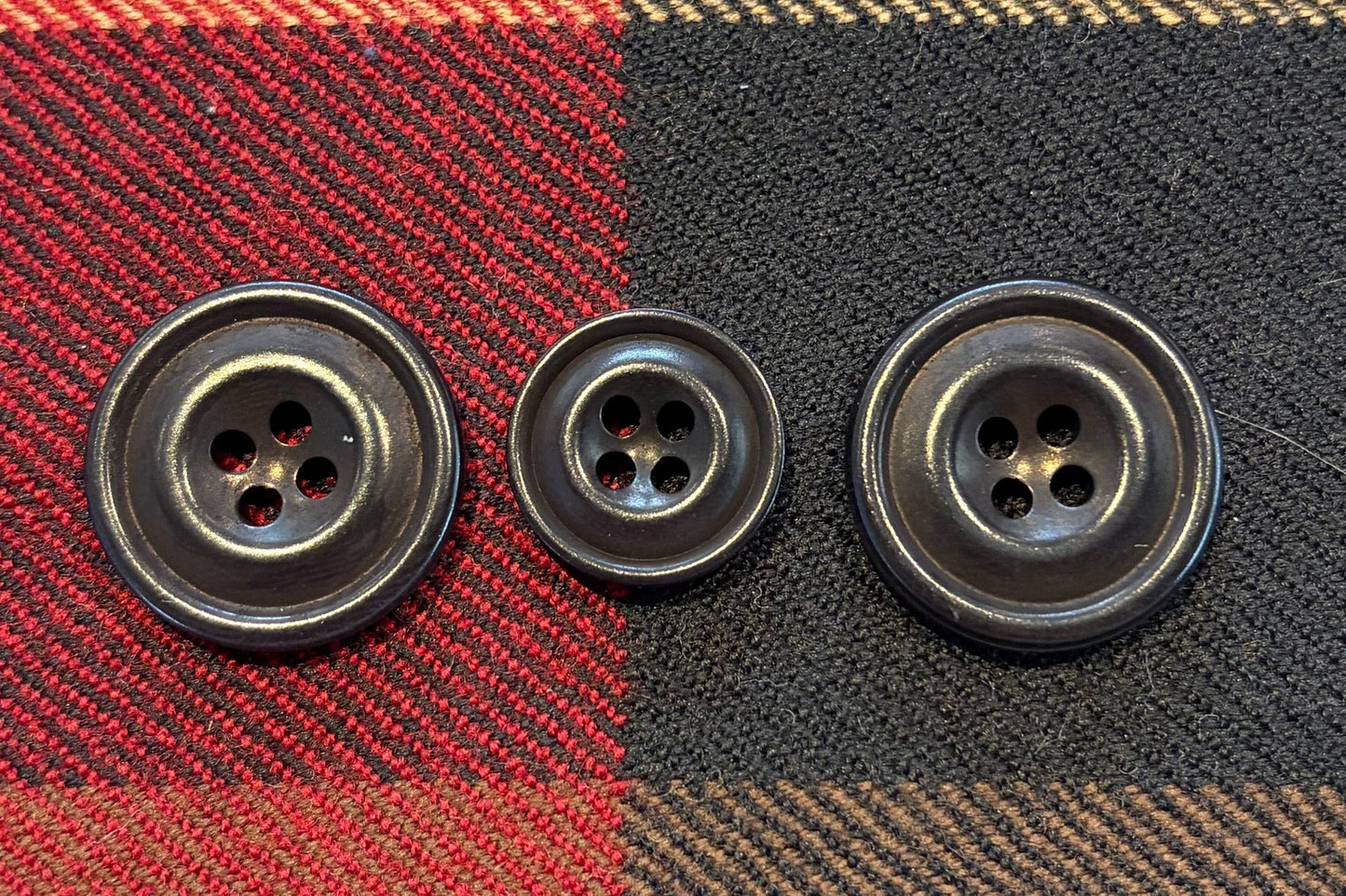 Three black buttons on a plaid fabric background